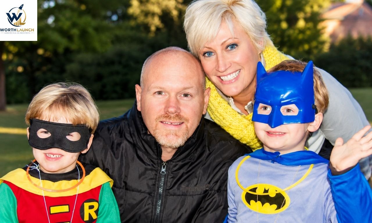 A family posing outdoors, with two children dressed in superhero costumes alongside their smiling parents.