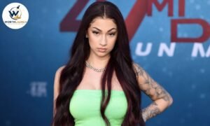 Young woman in a lime-green strapless outfit posing at a red-carpet event with long dark hair, tattoos, and a silver chain necklace.