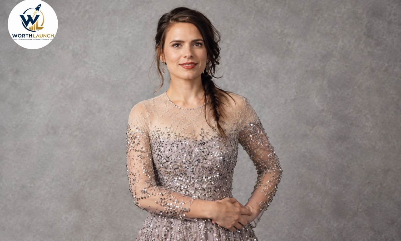 Hayley Atwell wearing a sparkling embellished gown with sheer sleeves and a side braid against a soft gray background.
