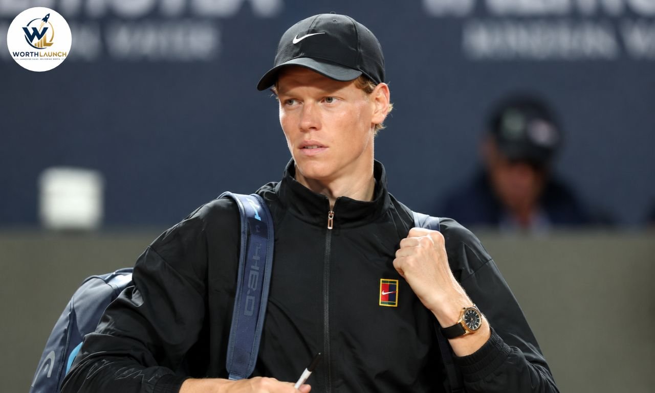 Jannik Sinner wearing a black tennis jacket and cap while carrying his tennis bag at a tournament.