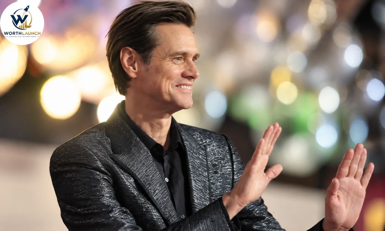 Jim Carrey smiling and gesturing with both hands at a glamorous event in a black suit.