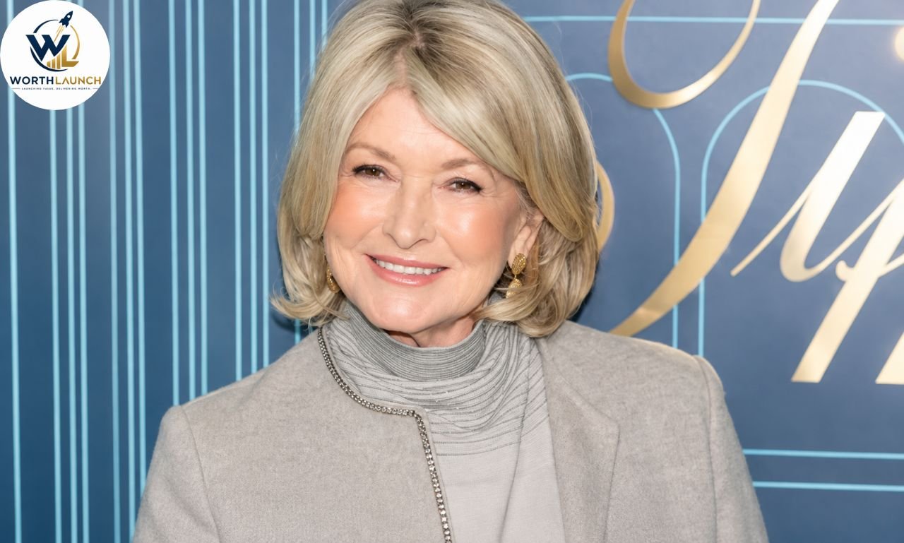 Martha Stewart smiling in a light-gray outfit at a professional event with a blue and gold backdrop.