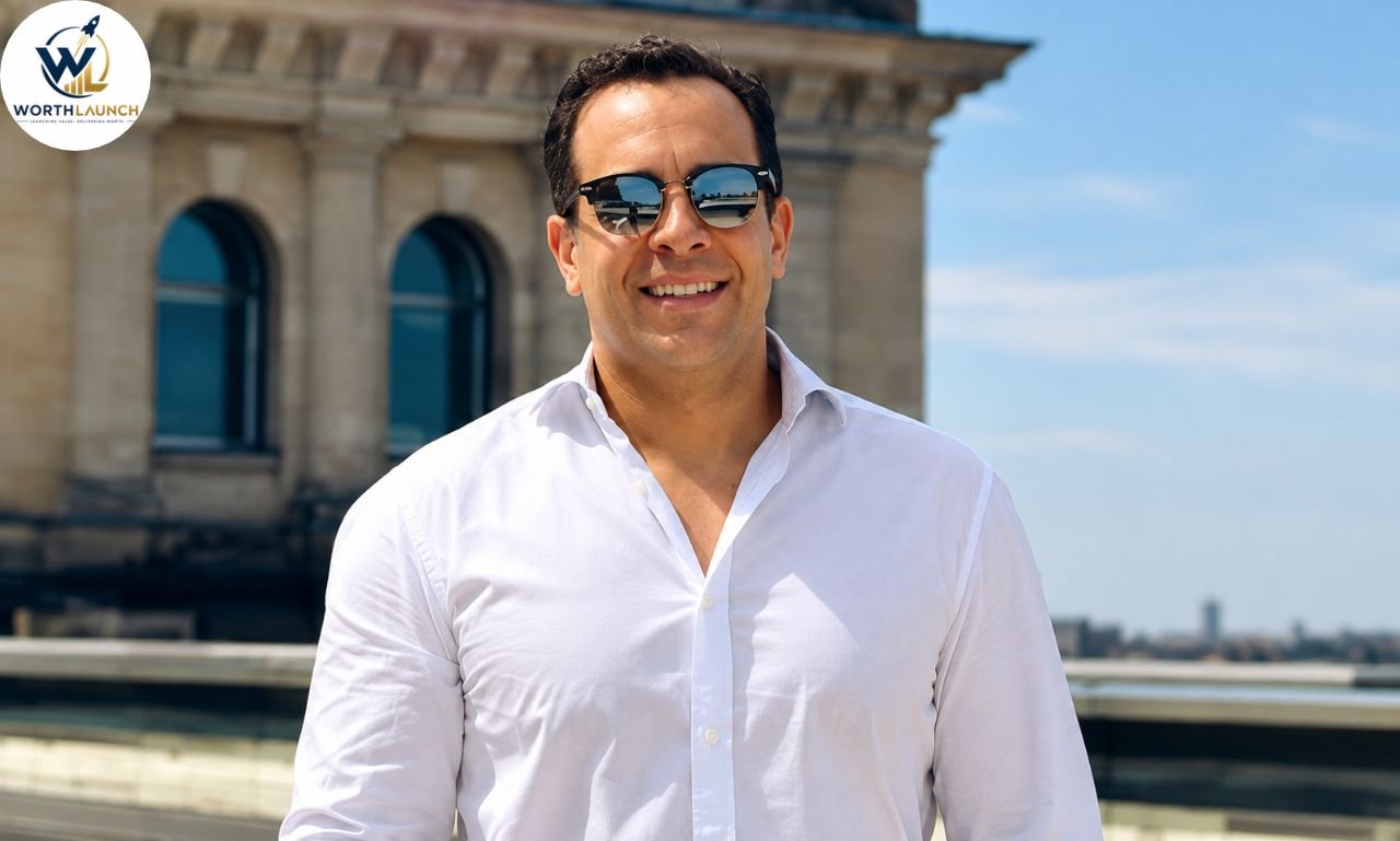 Smiling man wearing sunglasses and a white shirt outdoors in front of a historic building.