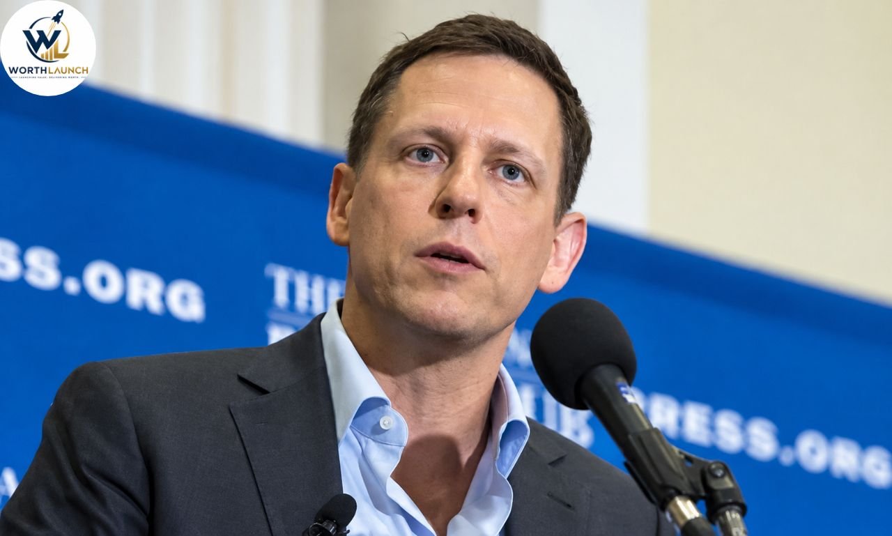 Man in a suit speaking into a microphone at a press conference with a blue backdrop.