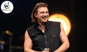 Morgan Wallenr performing on stage in a black sleeveless shirt, holding a microphone under warm stage lighting.