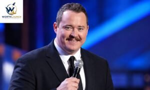 A man in a black suit and tie smiling at the camera on a brightly lit stage.