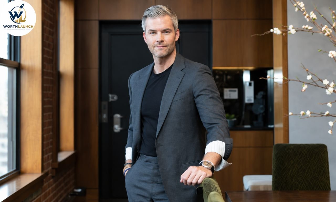 Silver-haired man in a gray suit posing confidently in a modern office with warm wood interiors and elegant décor.