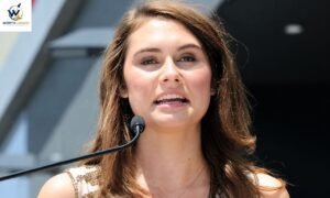 A young woman with brown hair speaks into a microphone at an outdoor event.