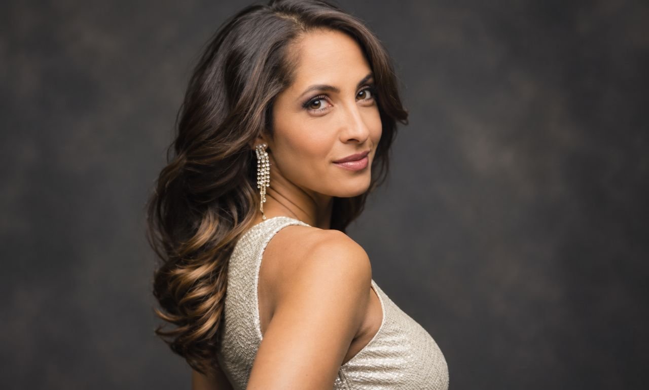 Christel Khalil in a champagne-colored outfit with long dark wavy hair and elegant earrings.