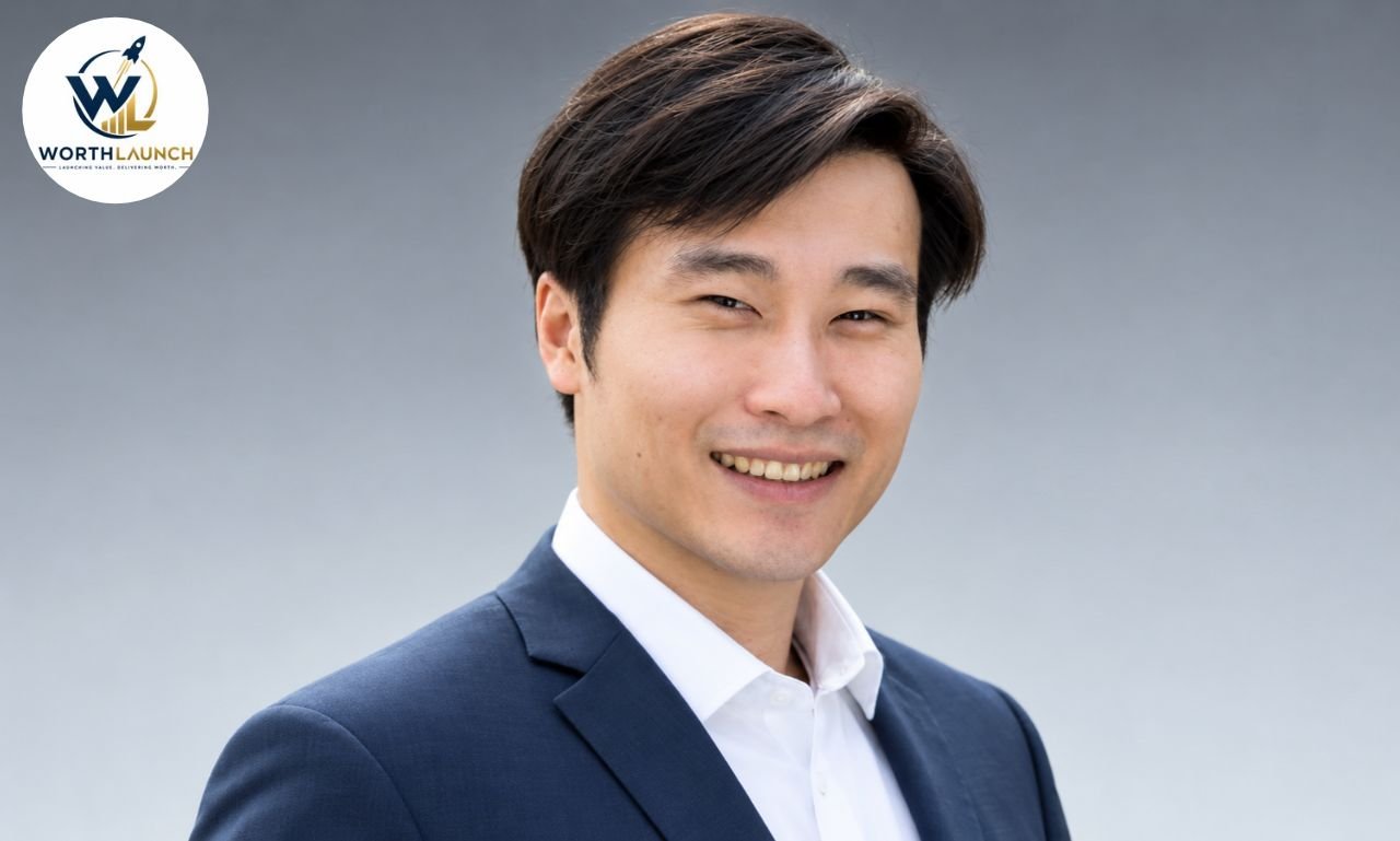 David Sun smiling in a navy blazer and white shirt against a soft gray background.