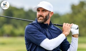 Dustin Johnson holding a golf club over his shoulders on a golf course, wearing a white cap and navy blue golf shirt.