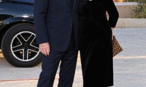 "Jonathan Banks and Gennera Gonzalez Cebian posing together outdoors in elegant black outfits, with a car and scenic desert mountains in the background."