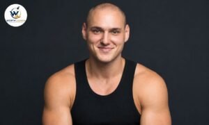 Leo Skepi in a black tank top posing for a professional studio portrait against a dark background.