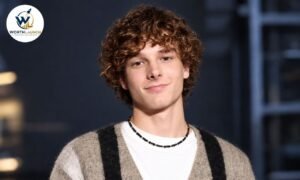 Mason Thames portrait with curly brown hair wearing a beige cardigan and white shirt.