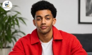 Miles Fowler wearing a red jacket and white shirt, posing for a professional portrait indoors.