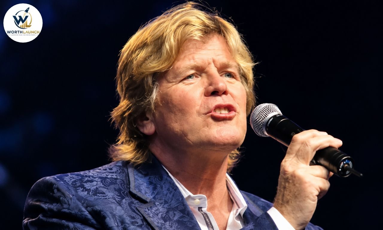 Peter Noone singing into a microphone during a live concert performance.