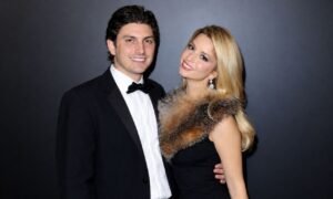 Ramzi Habibi posing in a black tuxedo beside a blonde woman in an elegant black dress at a red carpet event.