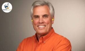 Verne Martell wearing an orange button-down shirt and yellow earplugs in a professional portrait.
