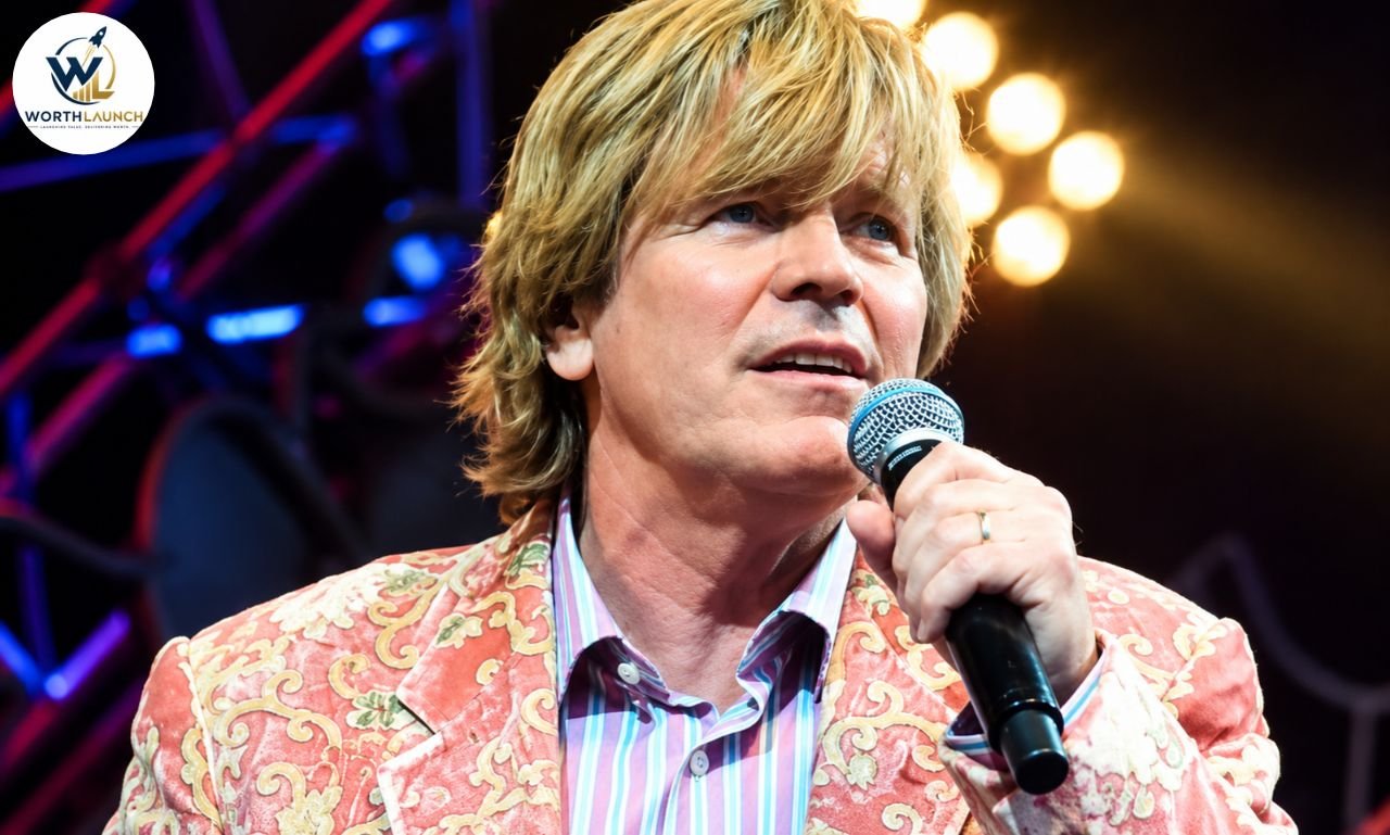 Peter Noone performing live on stage, singing into a microphone during a concert.